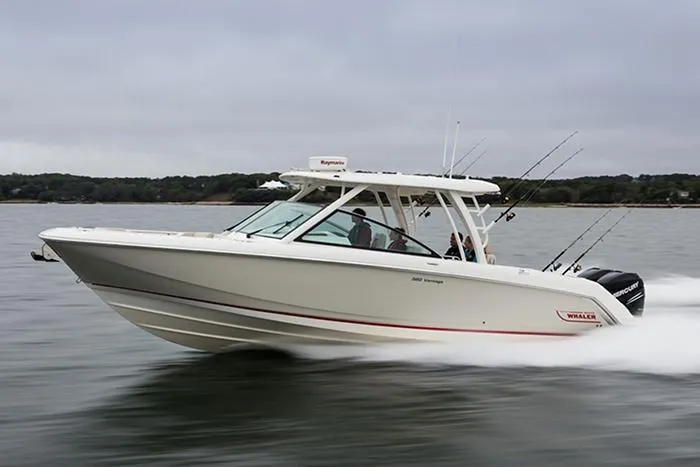 The Image of 2023 Boston Whaler 320 Vantage boat cruising on calm water near a shoreline. - 0