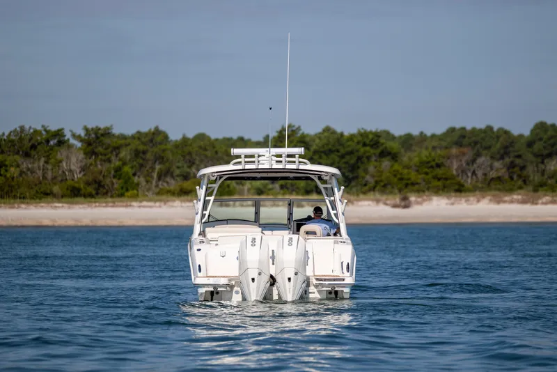 Slide: The Image of 2023 Boston Whaler 320 Vantage boat cruising on calm water near a sandy shoreline. - 12