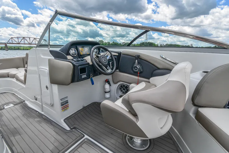 Slide: The Image of 2019 Crownline Eclipse E255 SURF boat interior with steering wheel and seating, under a cloudy sky. - 20
