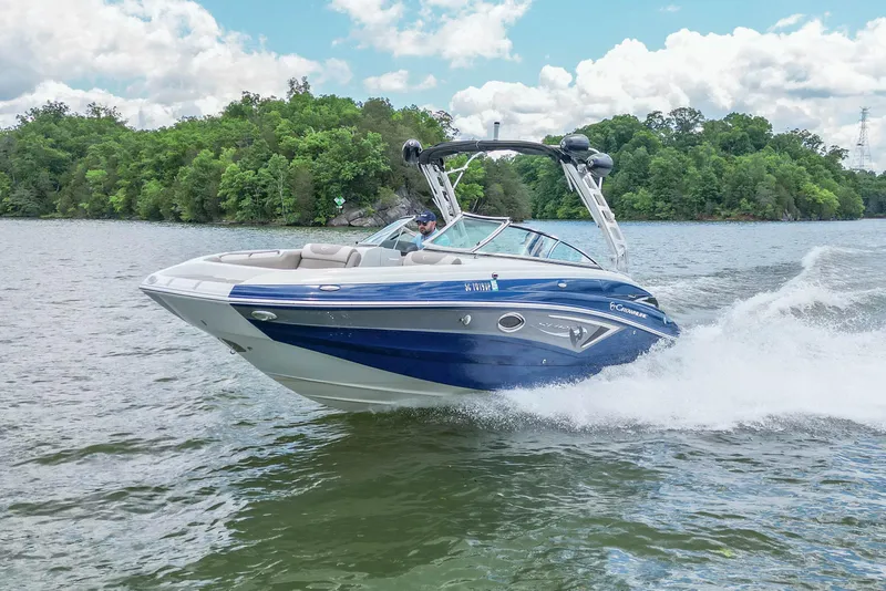 Slide: The Image of 2019 Crownline Eclipse E255 SURF boat cruising on a lake with lush green trees. - 4