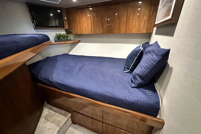 Slide: The Image of 2017 Viking 55 Convertible cabin with blue bedding, wooden cabinets, and a mounted TV. - 121