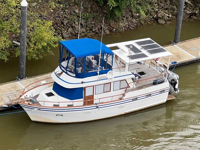 The Image of 1983 Lindmark 39 Trawler with blue canopy docked on a river. - 0