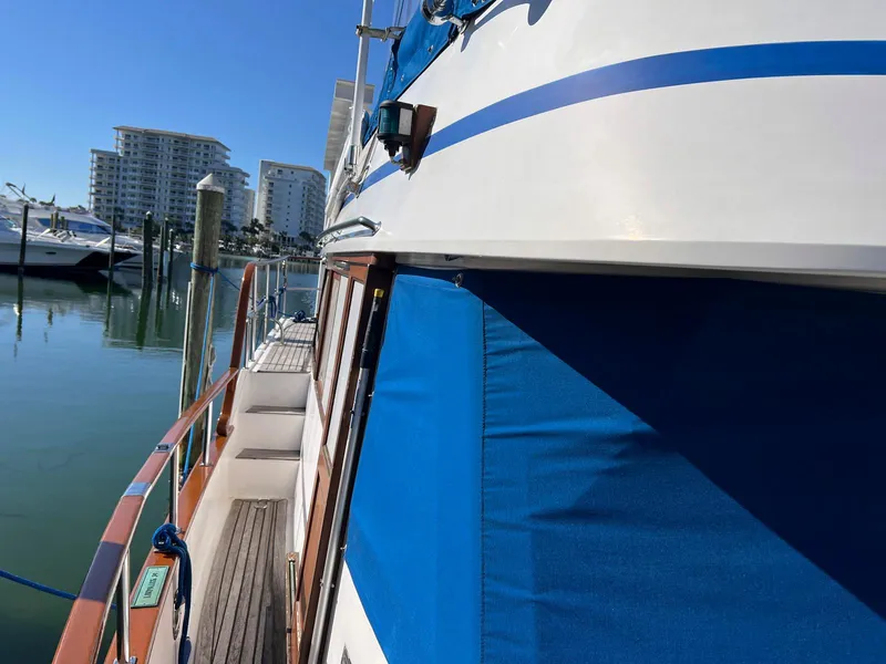 Slide: The Image of 1983 Lindmark 39 Trawler docked, featuring blue canvas and wooden deck, with buildings in background. - 31