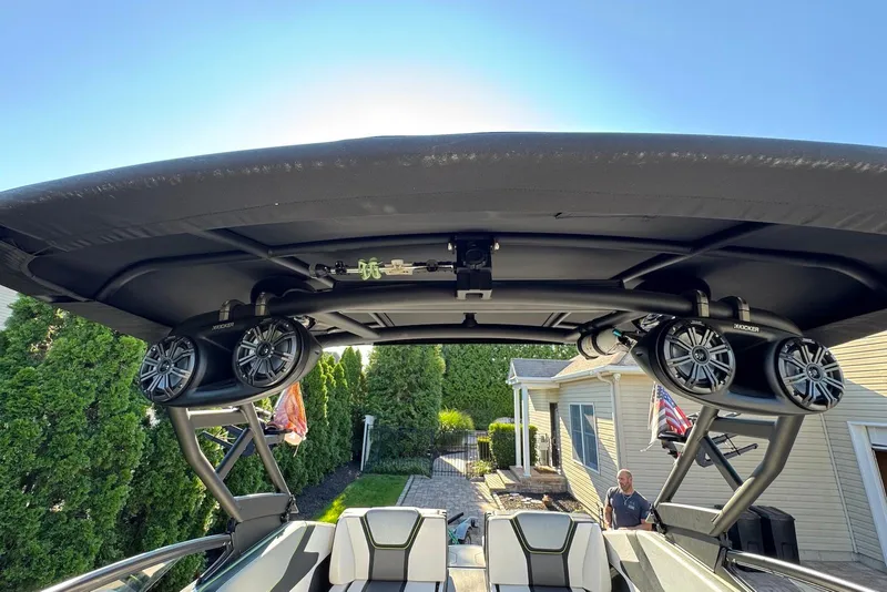 Slide: The Image of 2021 Yamaha Boats 255XD with speakers on canopy, parked near a house. - 24