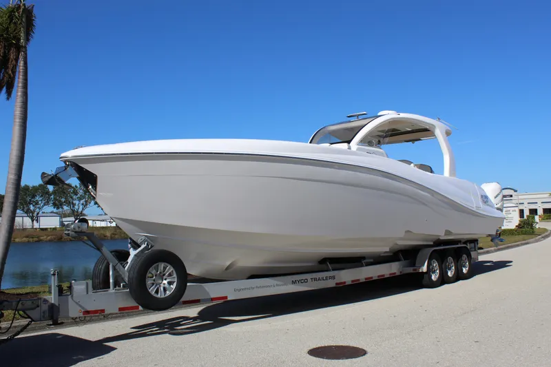 Slide: The Image of 2019 Deep Impact 399 Sport boat on trailer, parked near water under clear blue sky. - 0