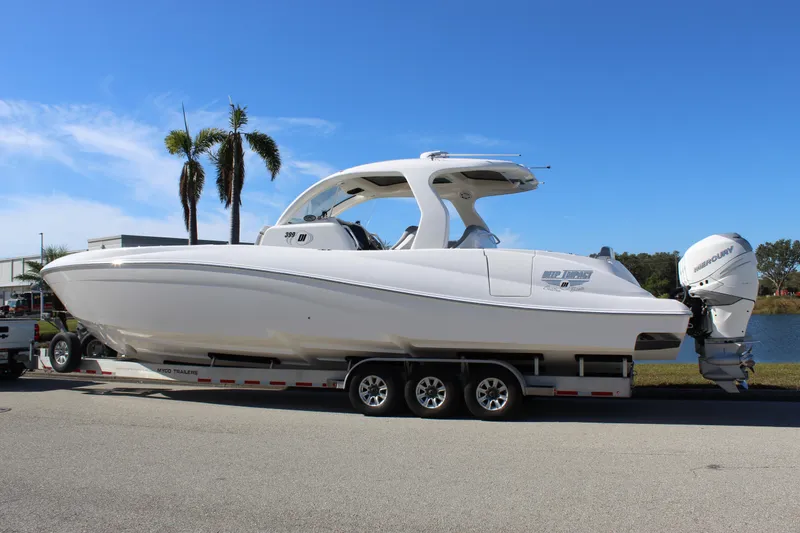 Slide: The Image of 2019 Deep Impact 399 Sport boat on trailer, parked near palm trees and water. - 10