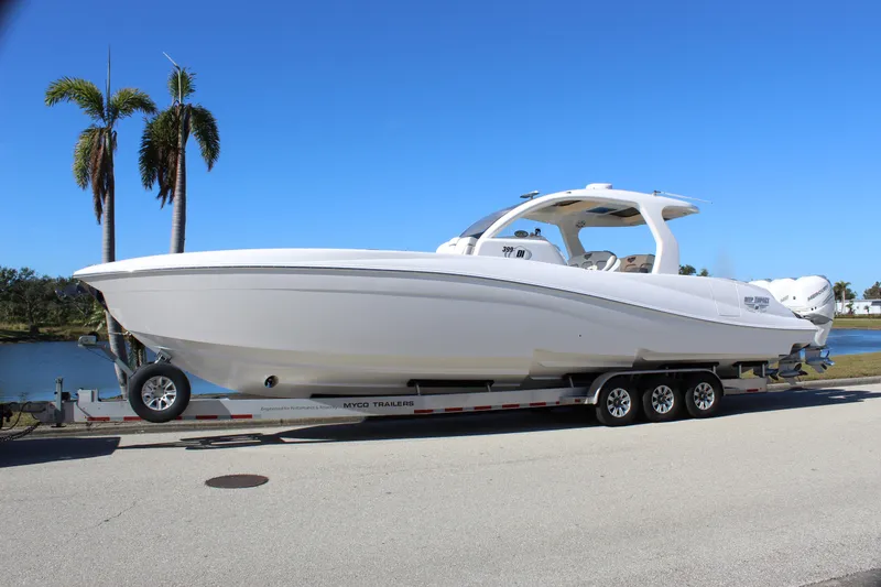 Slide: The Image of 2019 Deep Impact 399 Sport boat on trailer, parked near palm trees and water. - 6