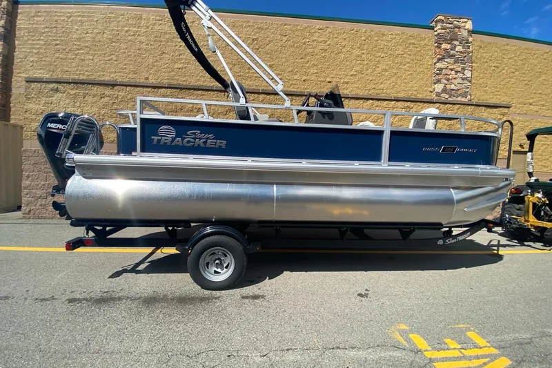 Slide: The Image of 2026 Sun Tracker Bass Buggy 18 DLX pontoon boat on trailer, parked outdoors. - 2