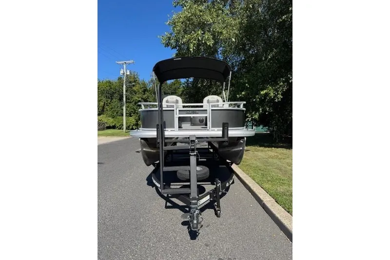 Slide: The Image of 2026 Sun Tracker Bass Buggy 16 XL Select pontoon boat on trailer, parked on a sunny street. - 2