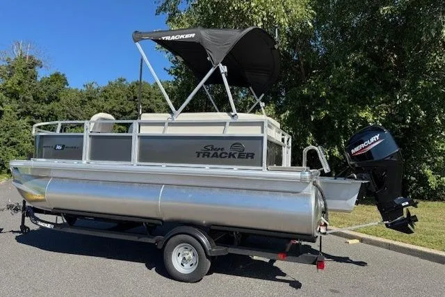 Slide: The Image of 2026 Sun Tracker Bass Buggy 16 XL Select pontoon boat on trailer, parked outdoors. - 6