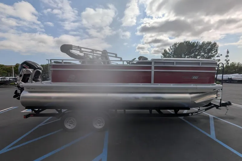 Slide: The Image of 2026 Sun Tracker SportFish 20 DLX pontoon boat on trailer under cloudy sky. - 2