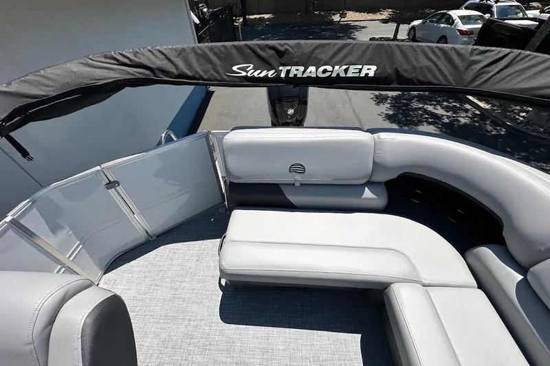 Slide: The Image of 2026 Sun Tracker Party Barge 20 DLX with gray seating and canopy, parked outdoors. - 16