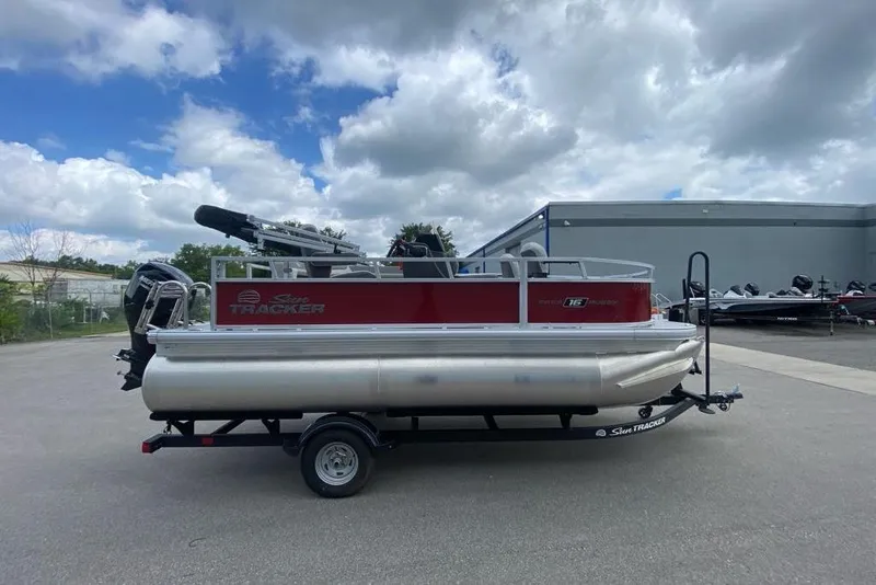 Slide: The Image of 2026 Sun Tracker Bass Buggy 16 XL Select pontoon boat on trailer, parked outdoors. - 2
