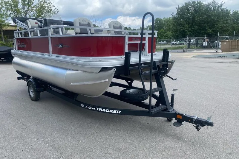 Slide: The Image of 2026 Sun Tracker Bass Buggy 16 XL Select pontoon boat on trailer, parked outdoors. - 3