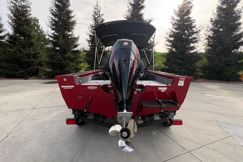 Slide: The Image of 2026 Tracker Targa V-19 Combo boat, rear view, parked outdoors with trees in background. - 58