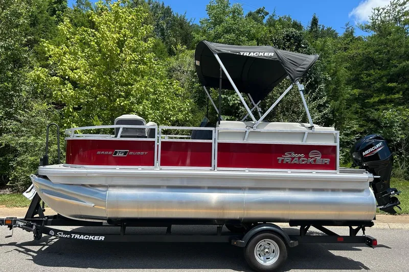 The Image of 2026 Sun Tracker Bass Buggy 16 XL Select pontoon boat on trailer, surrounded by trees. - 0