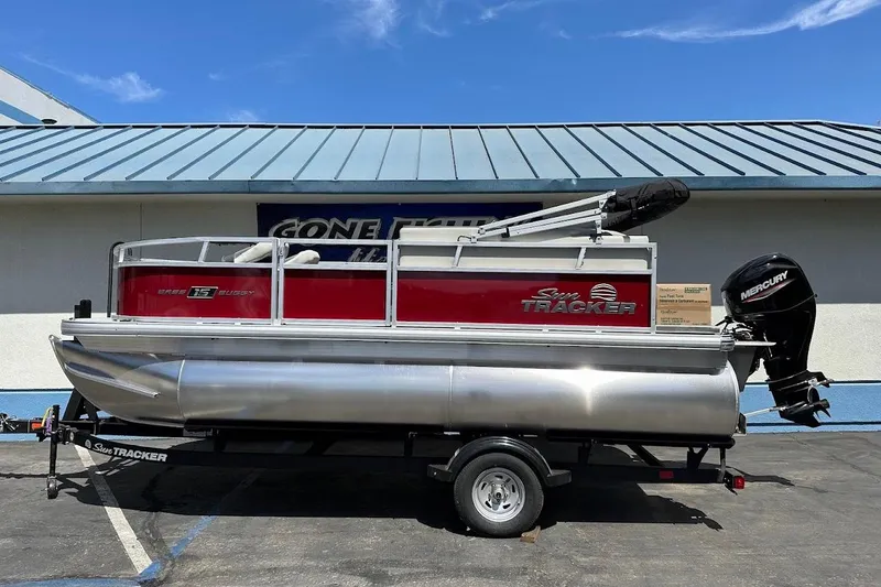 The Image of 2026 Sun Tracker Bass Buggy 16 XL Select pontoon boat on trailer, parked outdoors. - 0