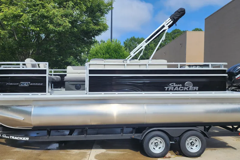 The Image of 2026 Sun Tracker Fishin' Barge 20 DLX pontoon boat on trailer, parked outdoors. - 0