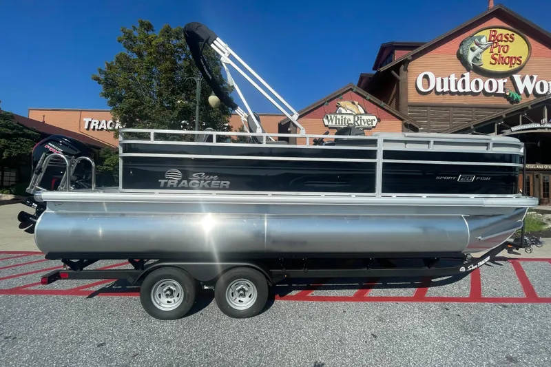 The Image of 2026 Sun Tracker SportFish 20 DLX pontoon boat outside Bass Pro Shops, "We Take Trades" sign visible. - 0