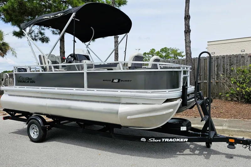 Slide: The Image of 2026 Sun Tracker Bass Buggy 18 DLX pontoon boat on trailer, parked outdoors. - 2