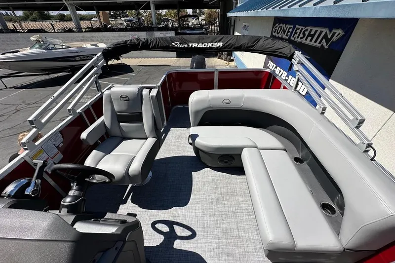 Slide: The Image of 2026 Sun Tracker Party Barge 18 DLX with gray seating and steering wheel, docked outdoors. - 12