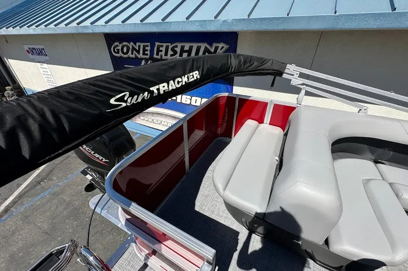 Slide: The Image of 2026 Sun Tracker Party Barge 18 DLX with seating and canopy, parked near a "Gone Fishing" sign. - 15
