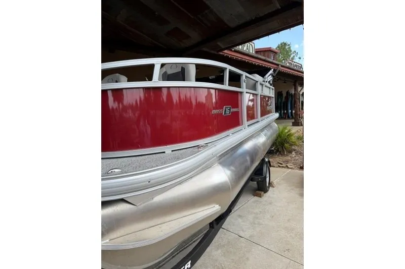 The Image of 2026 Sun Tracker Bass Buggy 16 XL Select pontoon boat, red exterior, parked on trailer. - 0