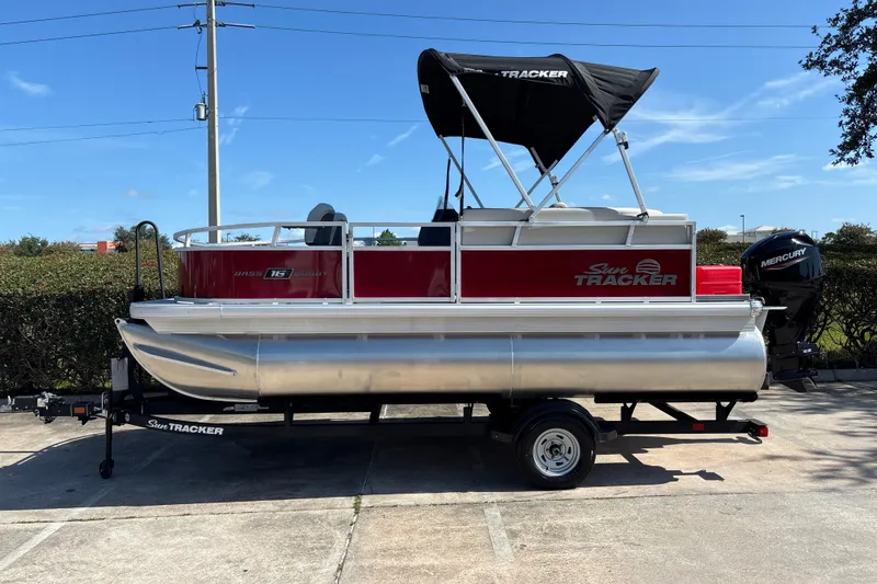 The Image of 2026 Sun Tracker Bass Buggy 16 XL Select pontoon boat on trailer, parked outdoors. - 0