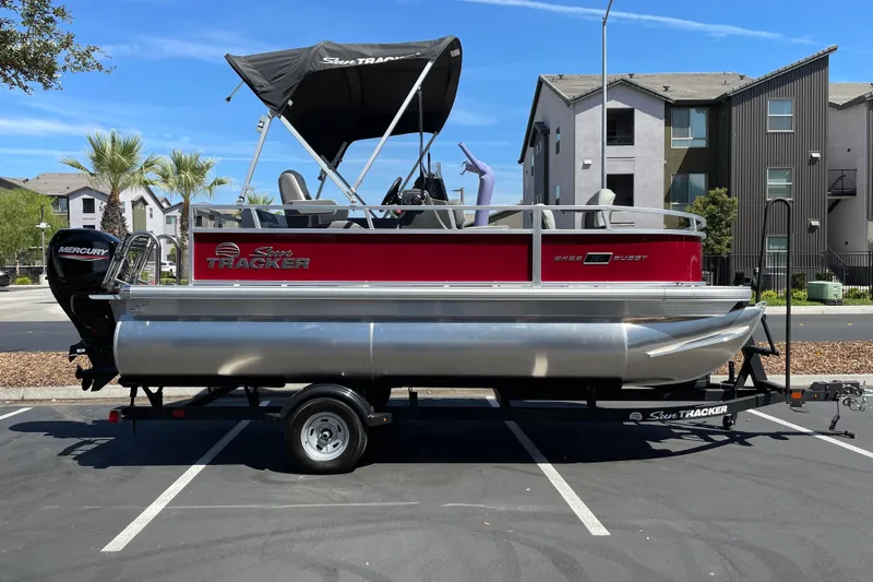 The Image of 2026 Sun Tracker Bass Buggy 16 XL Select pontoon boat on trailer in parking lot. - 0