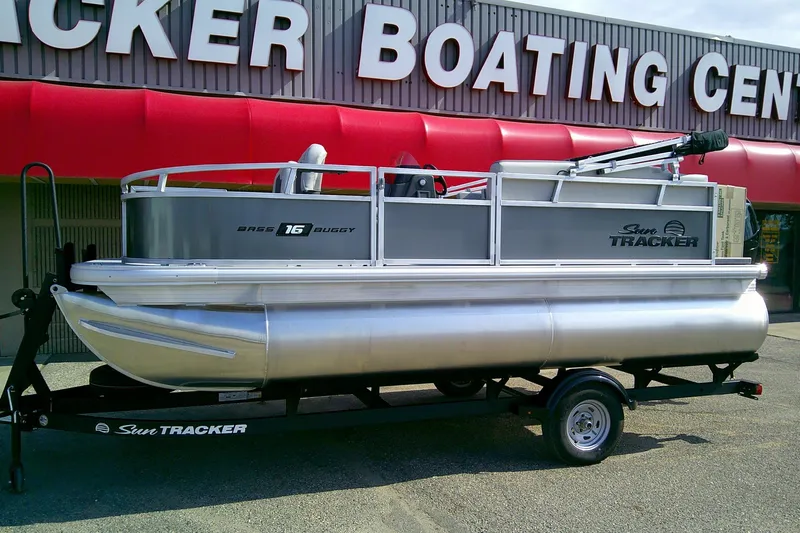 Slide: The Image of 2026 Sun Tracker Bass Buggy 16 XL Select pontoon boat on trailer outside dealership. - 2