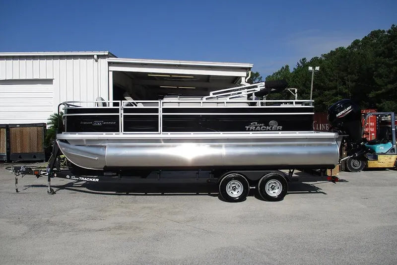 The Image of 2026 Sun Tracker Fishin' Barge 20 DLX pontoon boat on trailer, parked outside. - 1