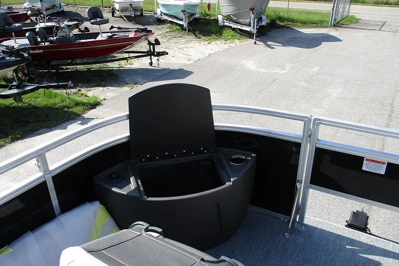 Slide: The Image of 2026 Sun Tracker Fishin' Barge 20 DLX interior with seating and storage, parked near other boats. - 12