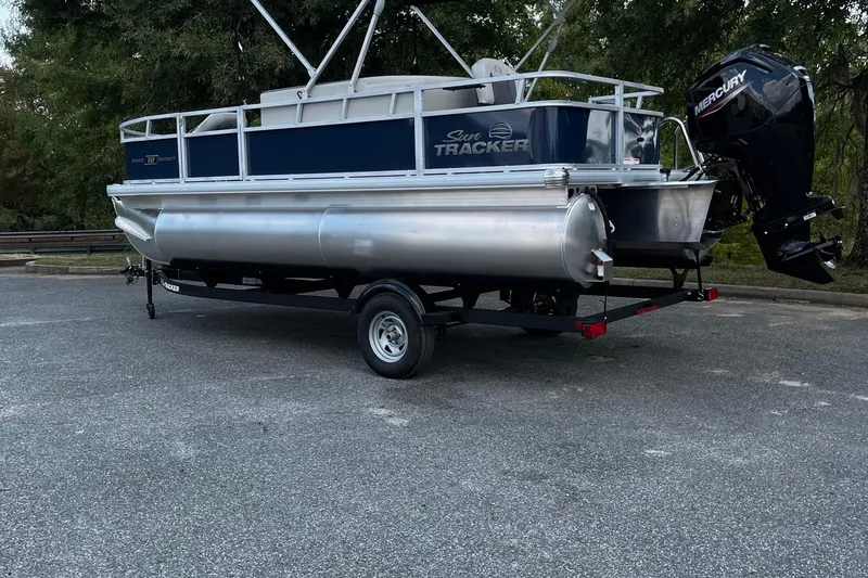 Slide: The Image of 2026 Sun Tracker Bass Buggy 18 DLX pontoon boat on trailer, parked outdoors. - 4