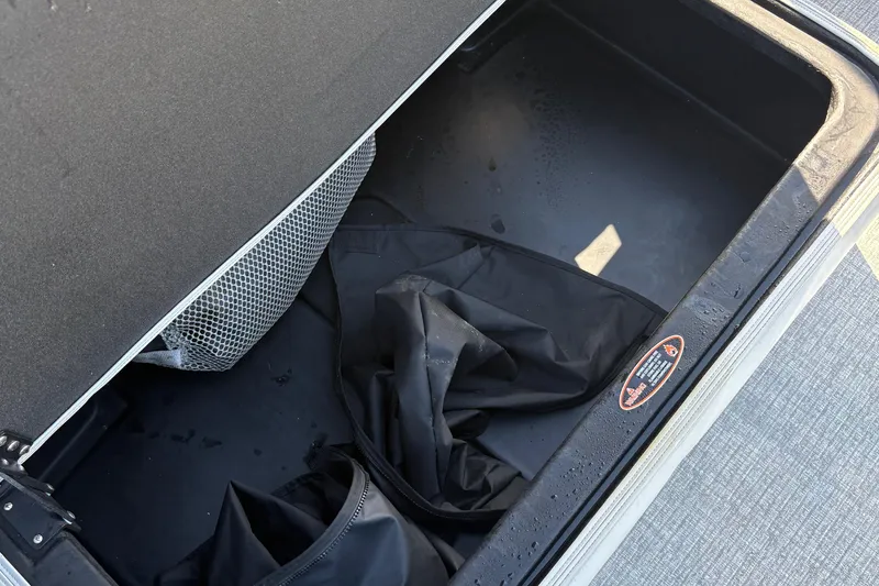 Slide: The Image of Open storage compartment in 2025 Harris Cruiser 230 boat, featuring mesh pocket and black cover. - 14