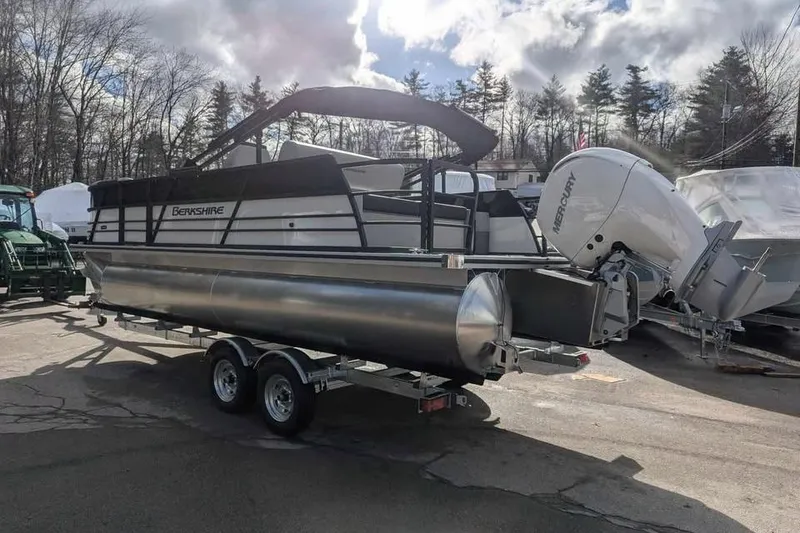 Slide: The Image of 2025 Berkshire 22UL LE pontoon boat on trailer, parked outdoors under cloudy sky. - 2