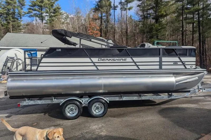 Slide: The Image of 2025 Berkshire 22UL LE pontoon boat on trailer, parked outdoors with trees in background. - 5