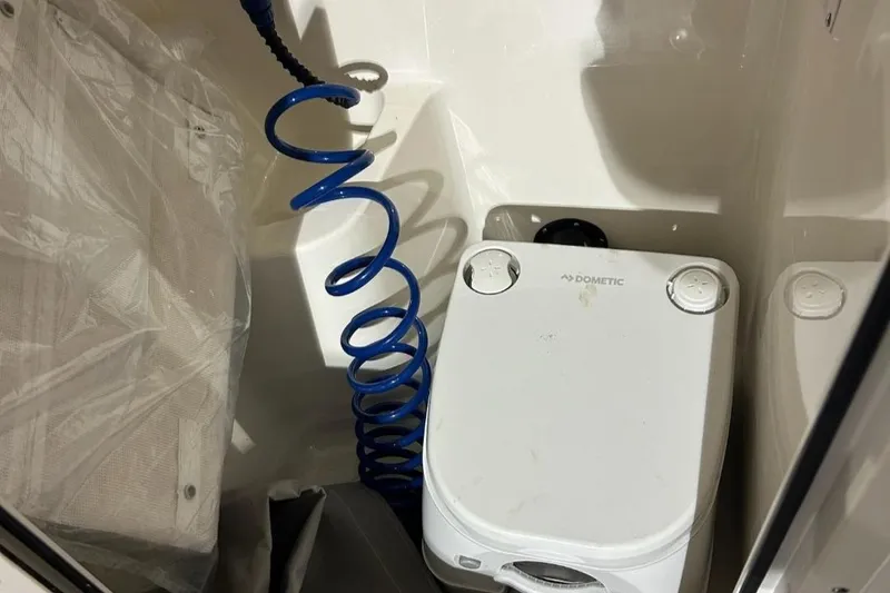 Slide: The Image of 2023 Key West 203 DFS boat interior with Dometic portable toilet and blue coiled hose. - 14