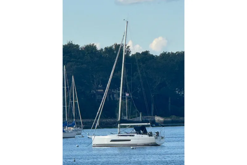 The Image of 2023 Dufour 37 sailboat anchored on calm water with forested background. - 0