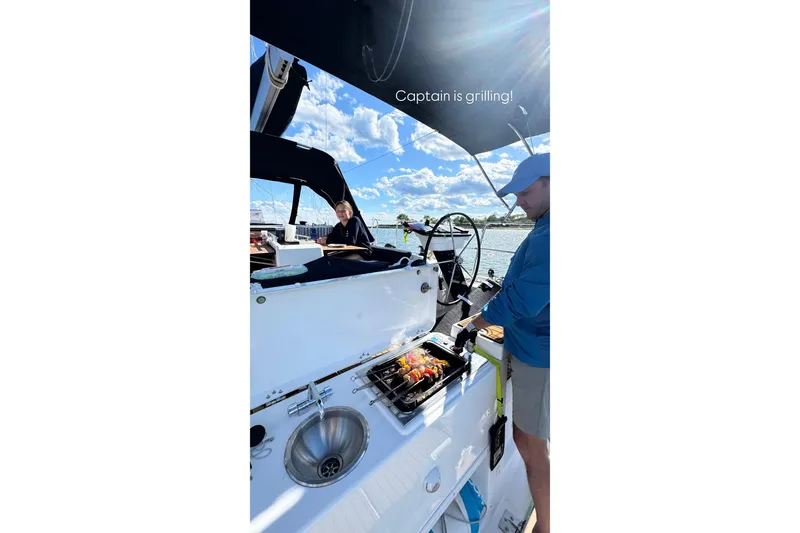 Slide: The Image of Man grilling on a 2023 Dufour 37 sailboat under sunny skies. - 24