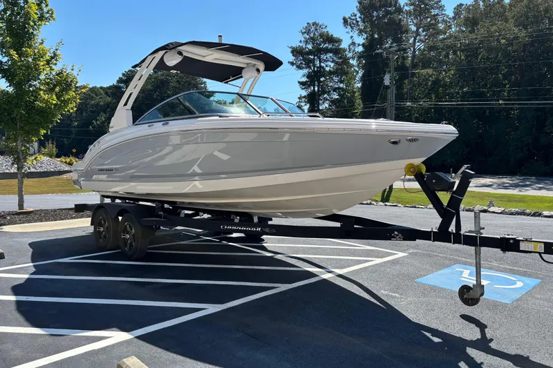 Slide: The Image of 2021 Chaparral 23 Surf boat on trailer in parking lot, surrounded by trees. - 2