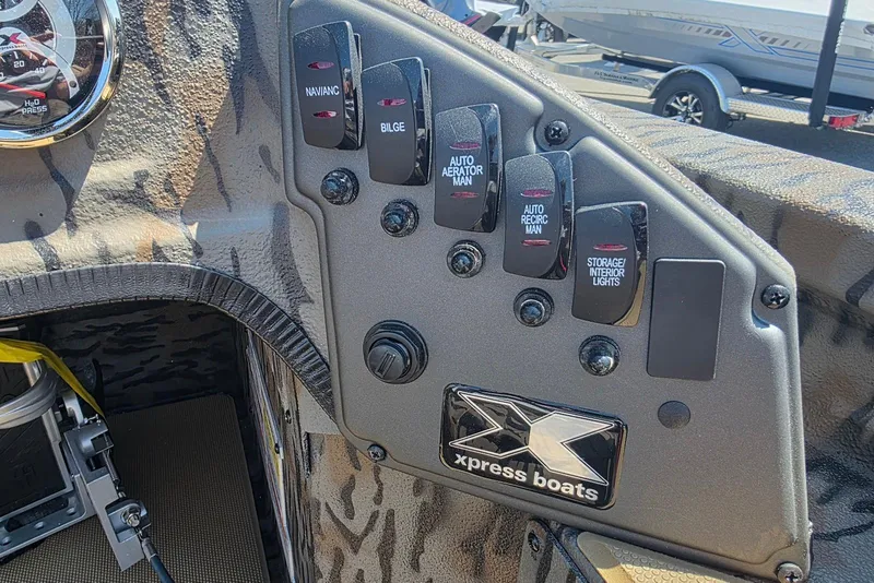 Slide: The Image of Control panel of 2026 Xpress H20 Bass boat with various switches and logo. - 23