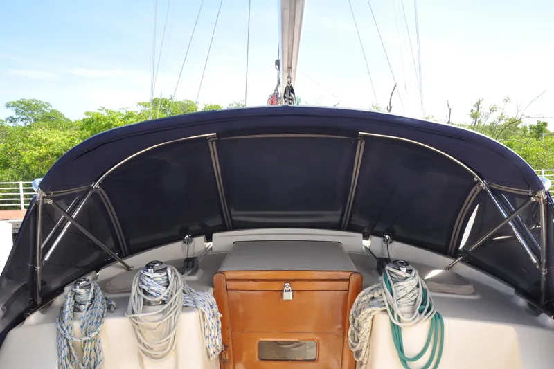 Slide: The Image of 2002 Island Packet 420 sailboat cockpit with ropes and canopy, docked near greenery. - 10