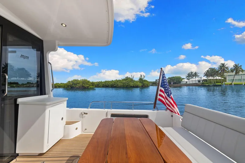 Slide: The Image of 2024 MJM 42 yacht deck with American flag, wooden table, and scenic water view. - 10
