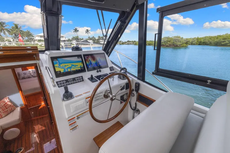 Slide: The Image of 2024 MJM 42 yacht helm with navigation screens, overlooking serene waterway and lush greenery. - 25