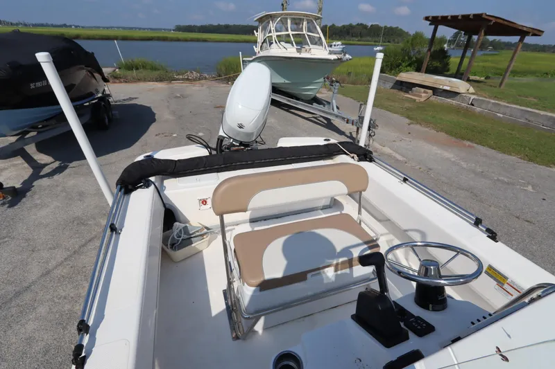 Slide: The Image of 2022 Sundance DX22 boat interior with steering wheel and seating, parked near a scenic waterway. - 9