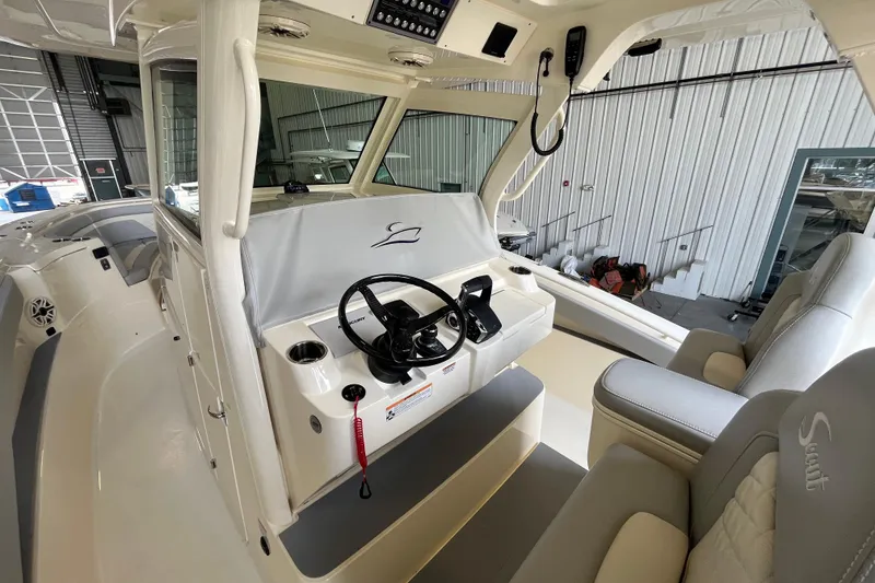Slide: The Image of 2026 Scout 330 LXF boat interior with steering wheel and seating in a marina setting. - 16