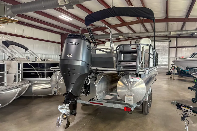 Slide: The Image of 2026 Trifecta 24UL CS pontoon boat with powerful outboard motor in showroom. - 2