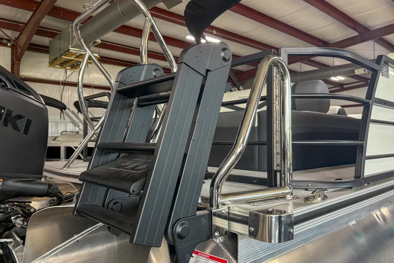 Slide: The Image of 2026 Trifecta 24UL CS pontoon boat with a foldable ladder and railing in a showroom. - 3