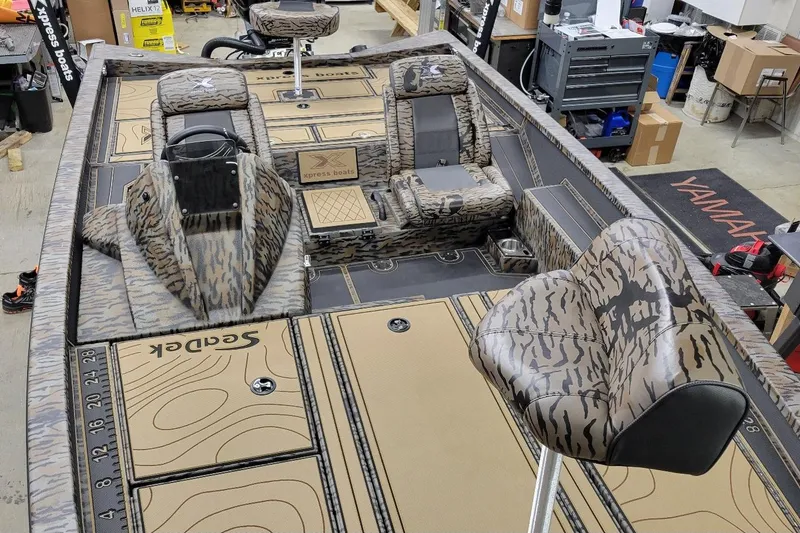 Slide: The Image of 2026 Xpress X19 Pro boat interior with camo seats and deck, in a workshop setting. - 7
