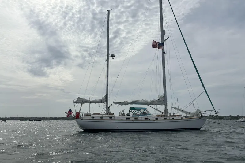 The Image of 1984 Shannon 51' Center Cockpit sailboat on water, cloudy sky, American flag. - 0